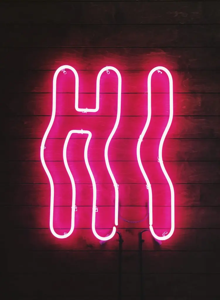 Pink neon sign shaped to spell “HI” on a dark wooden background.